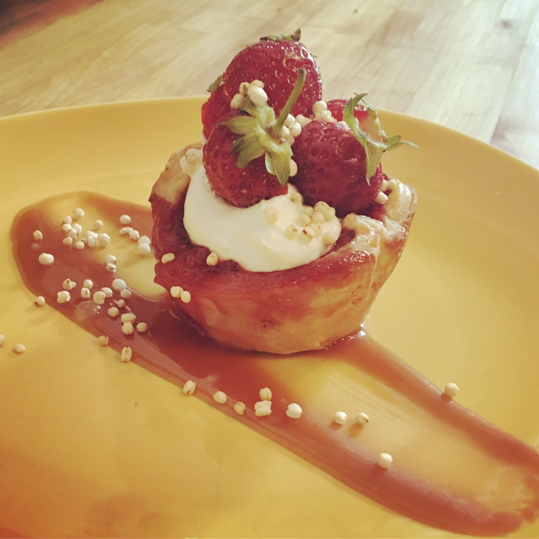A dessert on a yellow plate with strawberries, whipped cream, and a sauce.