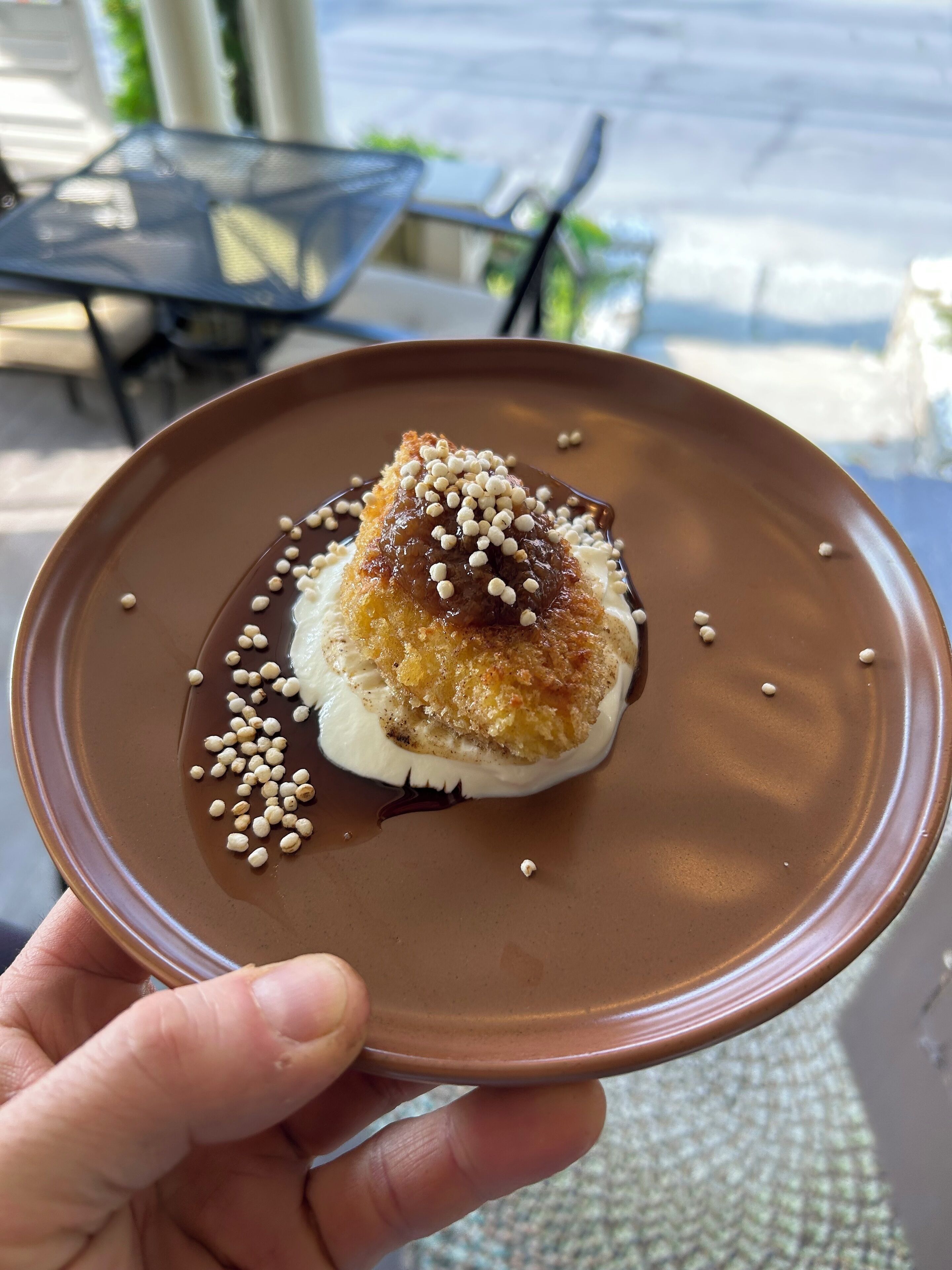 A dessert on a brown plate with a hand holding it.