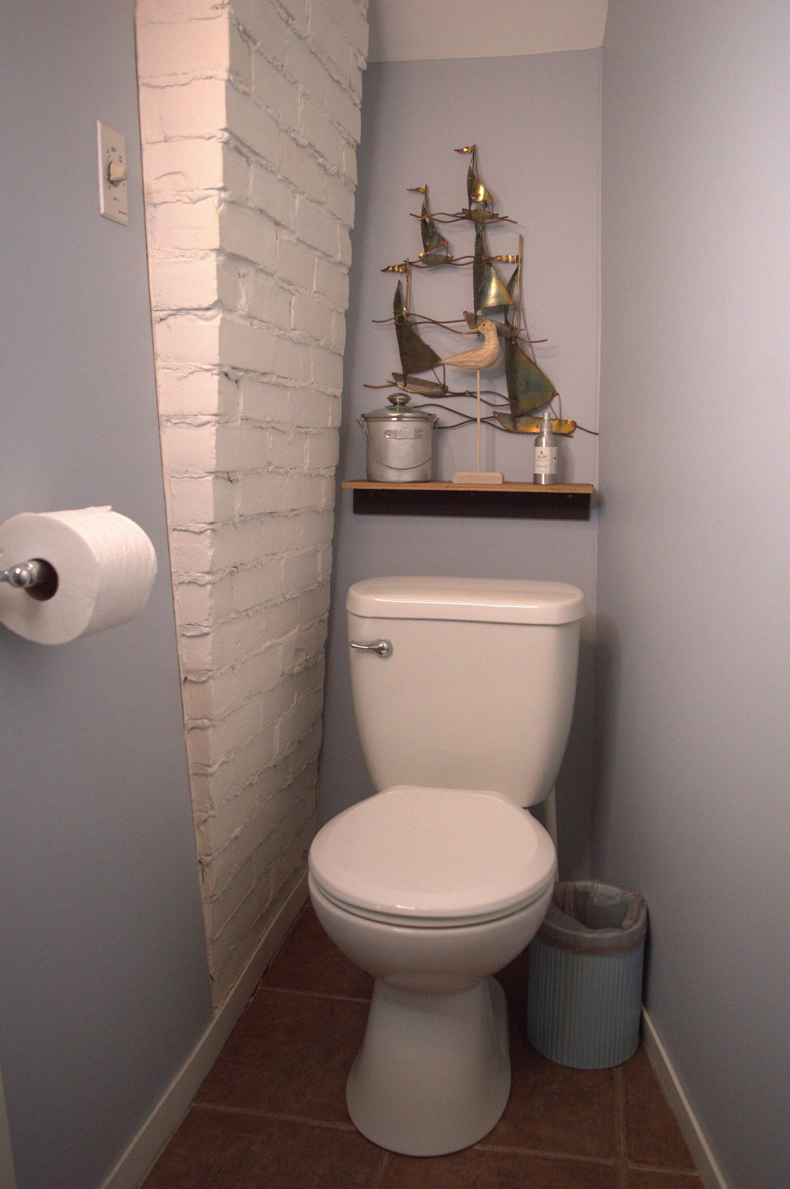 Un baño con un inodoro blanco, un rollo de papel higiénico, un bote de basura y una escultura metálica decorativa en un estante sobre el inodoro.