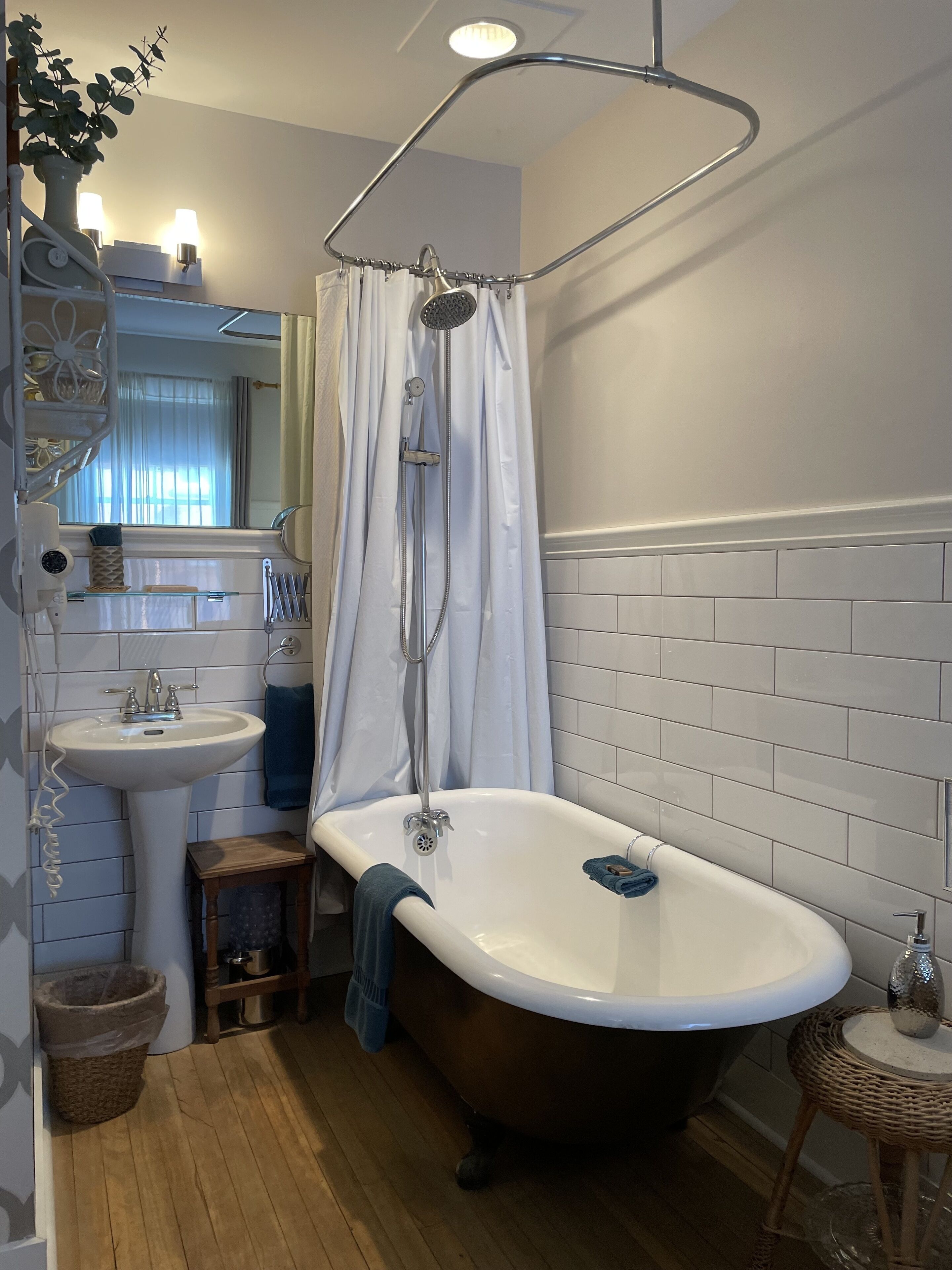 Ein Badezimmer mit freistehender Badewanne, einem Waschbecken auf Säule, einer Duschkabine mit Vorhang und einem Spiegel über dem Waschbecken.