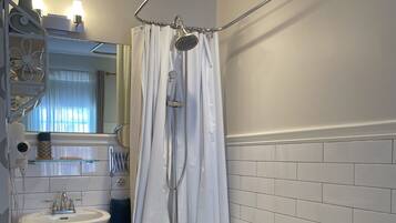 Ein Badezimmer mit freistehender Badewanne, einem Waschbecken auf Säule, einer Duschkabine mit Vorhang und einem Spiegel über dem Waschbecken.