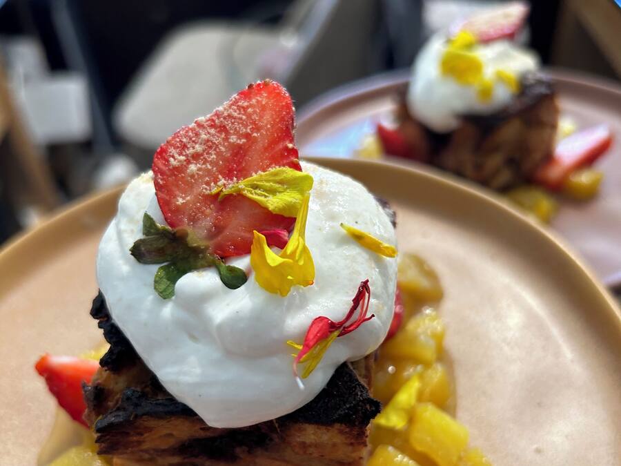 Un postre con un huevo pochado, fresas y mango en un plato.