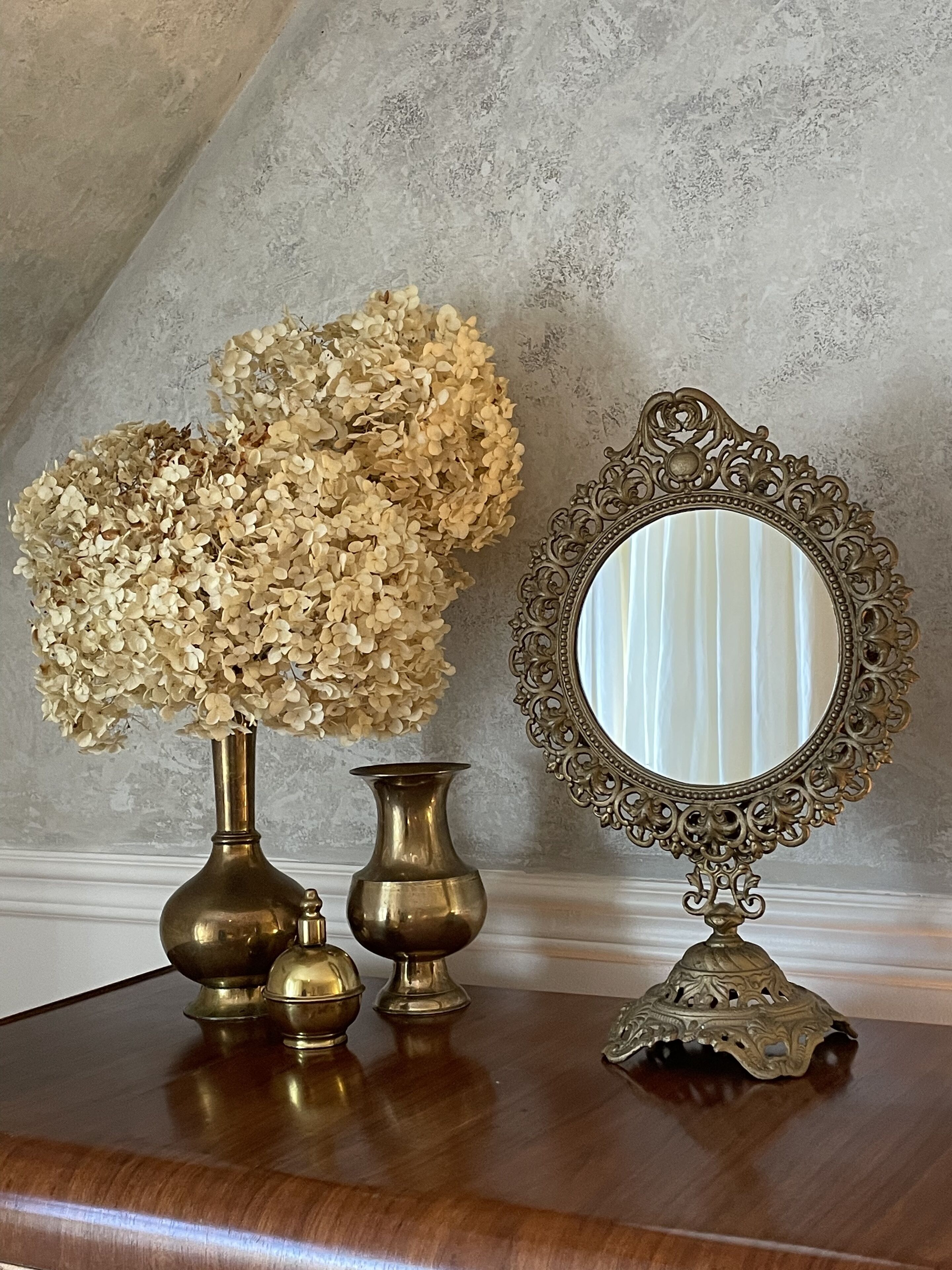 Un aparador de madera con tres jarrones de bronce y un espejo con marco decorado.