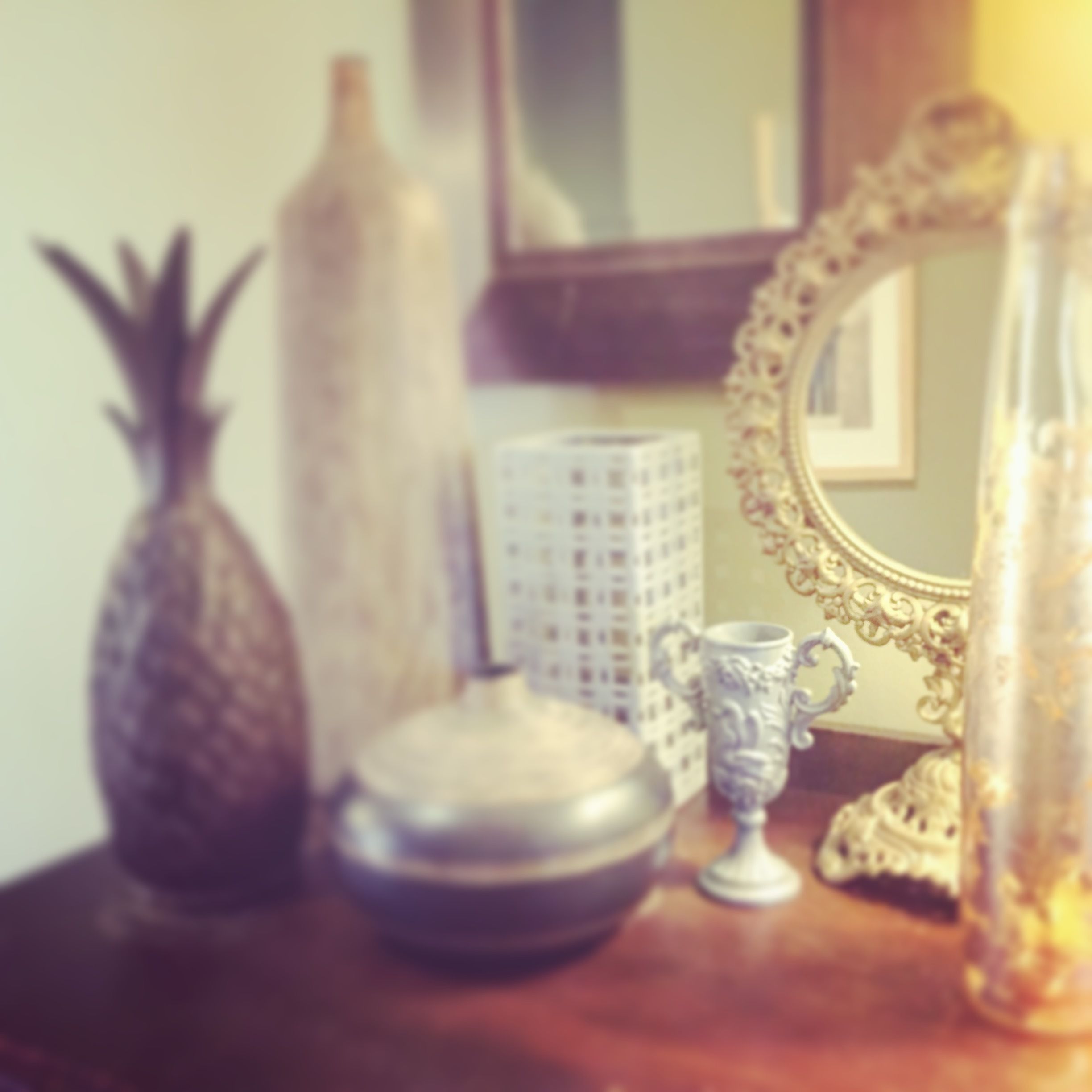 Een houten tafel met een ananas, een witte vaas, een zilveren beker en een glazen fles.