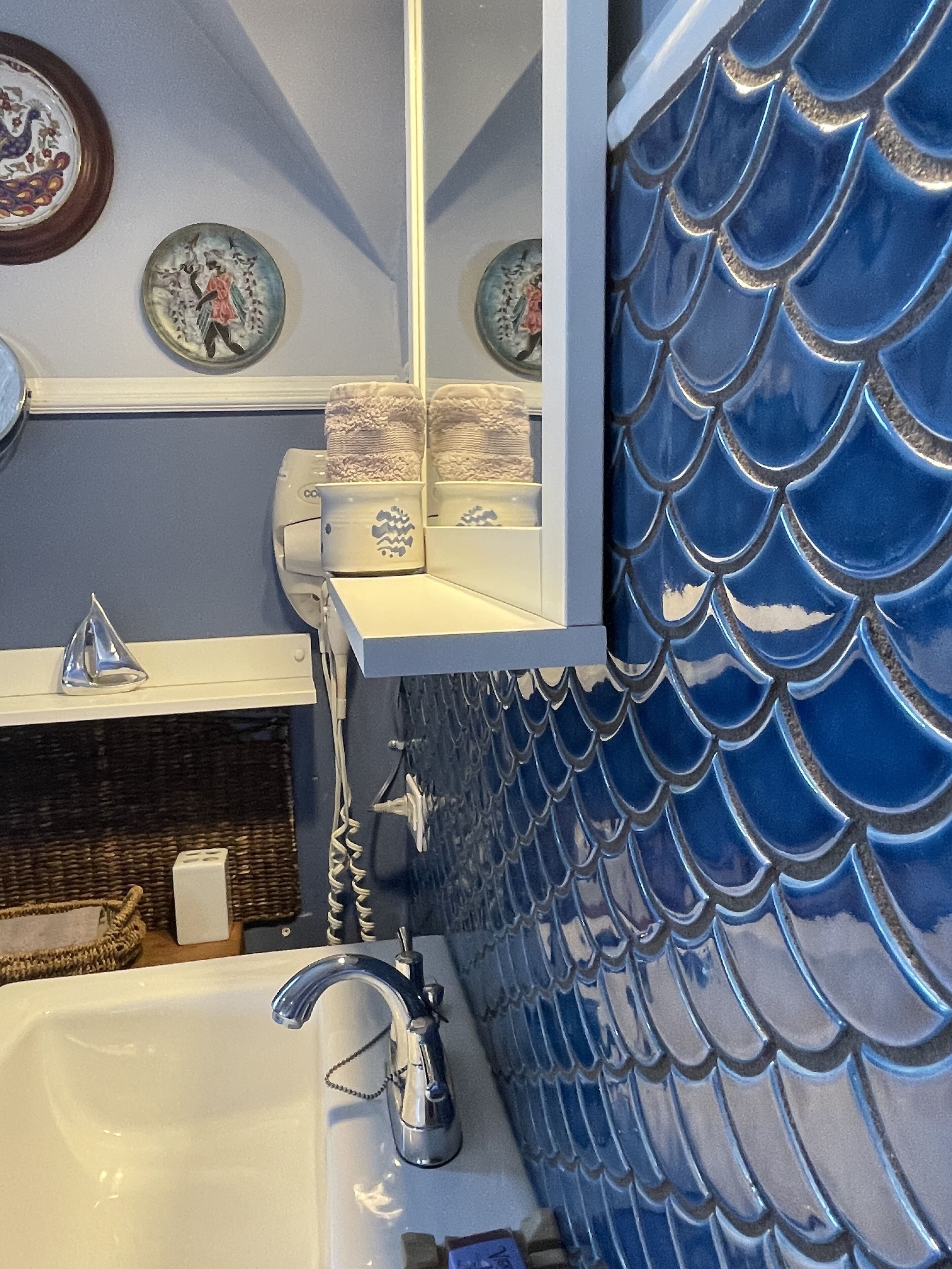 Un baño con salpicadero de azulejos con escamas de pez azul, un lavabo blanco y un espejo sobre él.