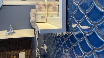 Une salle de bain avec un mur recouvert de carreaux bleus imitant des écailles de poisson, un lavabo blanc et un miroir au-dessus du lavabo.