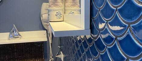 Un baño con salpicadero de azulejos con escamas de pez azul, un lavabo blanco y un espejo sobre él.