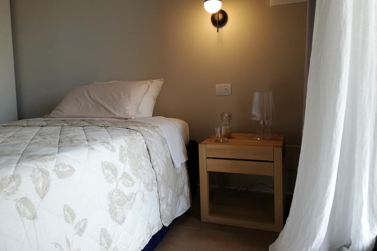 Une chambre à coucher avec un lit, une table de chevet avec une lampe, un verre et un interrupteur au mur.