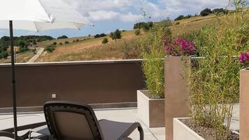 A rooftop terrace with a lounge chair, an umbrella, and planters with flowers.