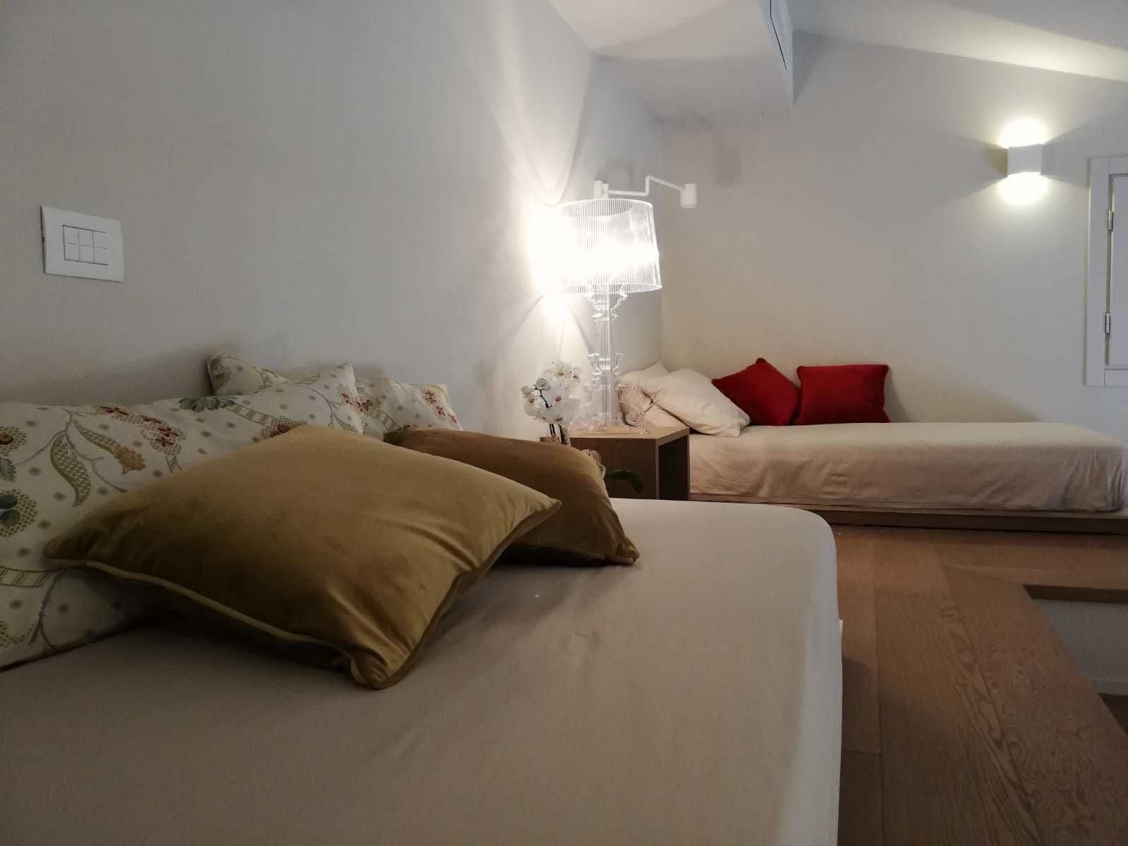 Une chambre à coucher avec un lit, deux oreillers, une table de chevet, une lampe et un luminaire fixé au mur.