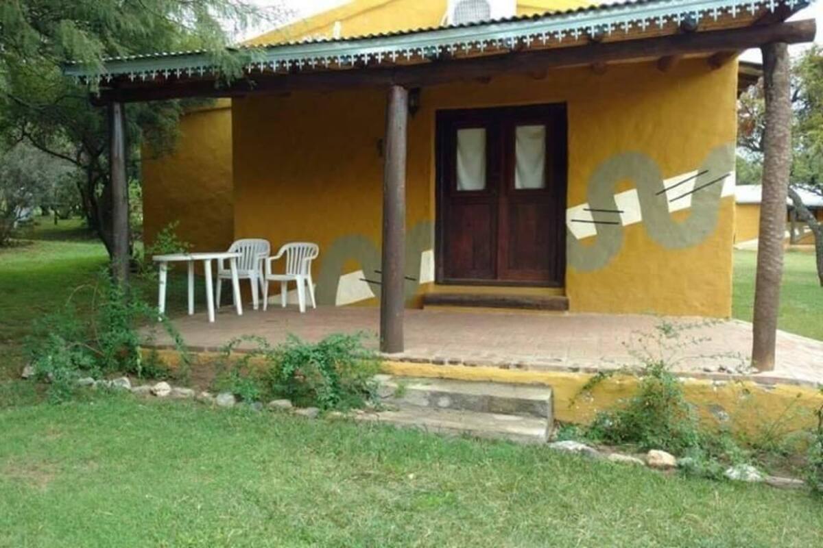 A yellow building with a porch, two white plastic chairs, and a wooden door.