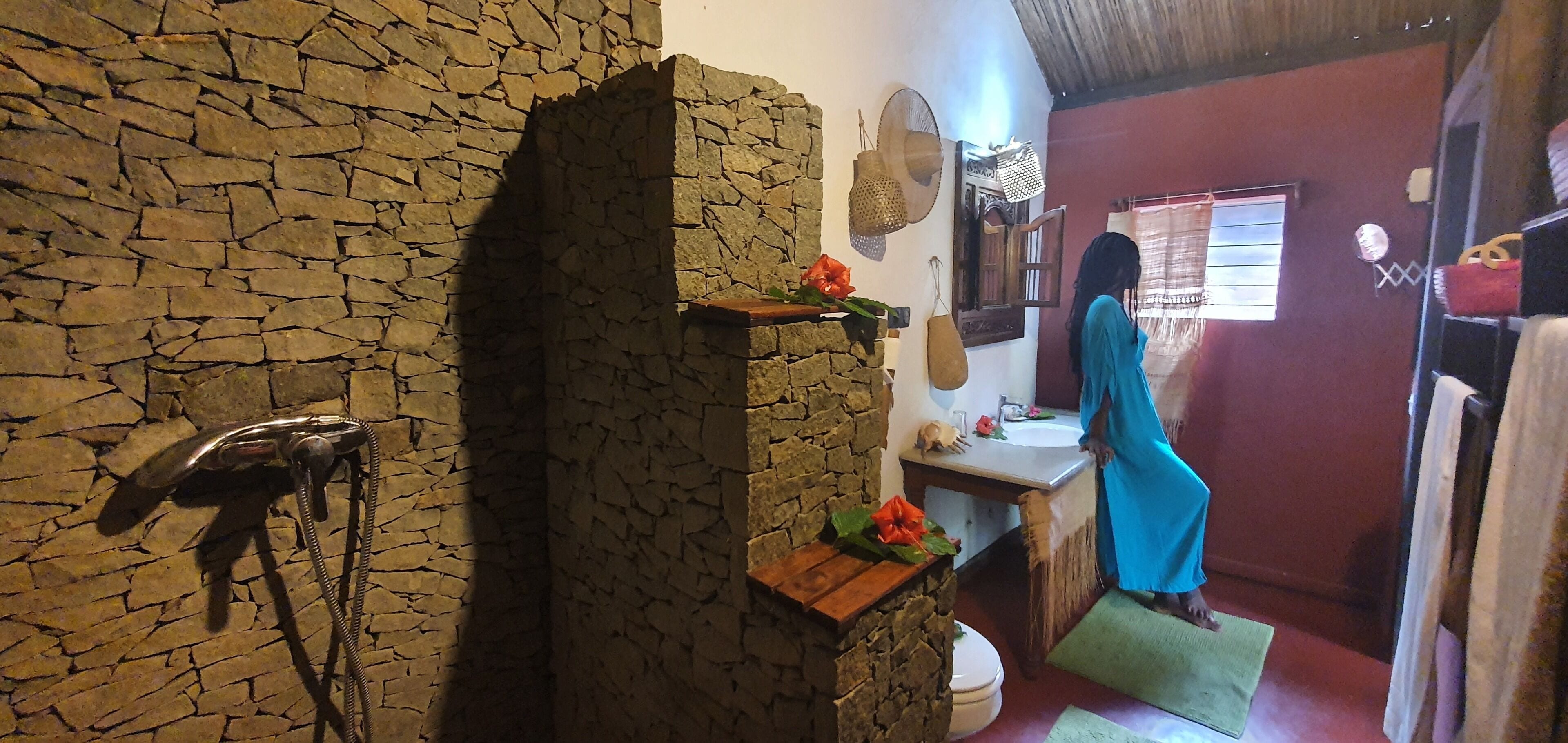 Un baño de paredes de piedra con ducha, lavabo y espejo.