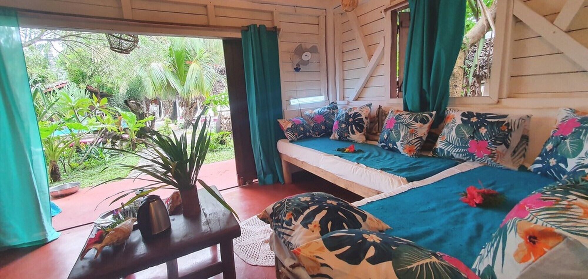 Una habitación con una cama, una mesa con una planta y vistas al verde exterior.
