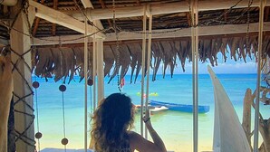 Vista desde una estructura de madera con techo de paja, con vista al mar y embarcaciones.