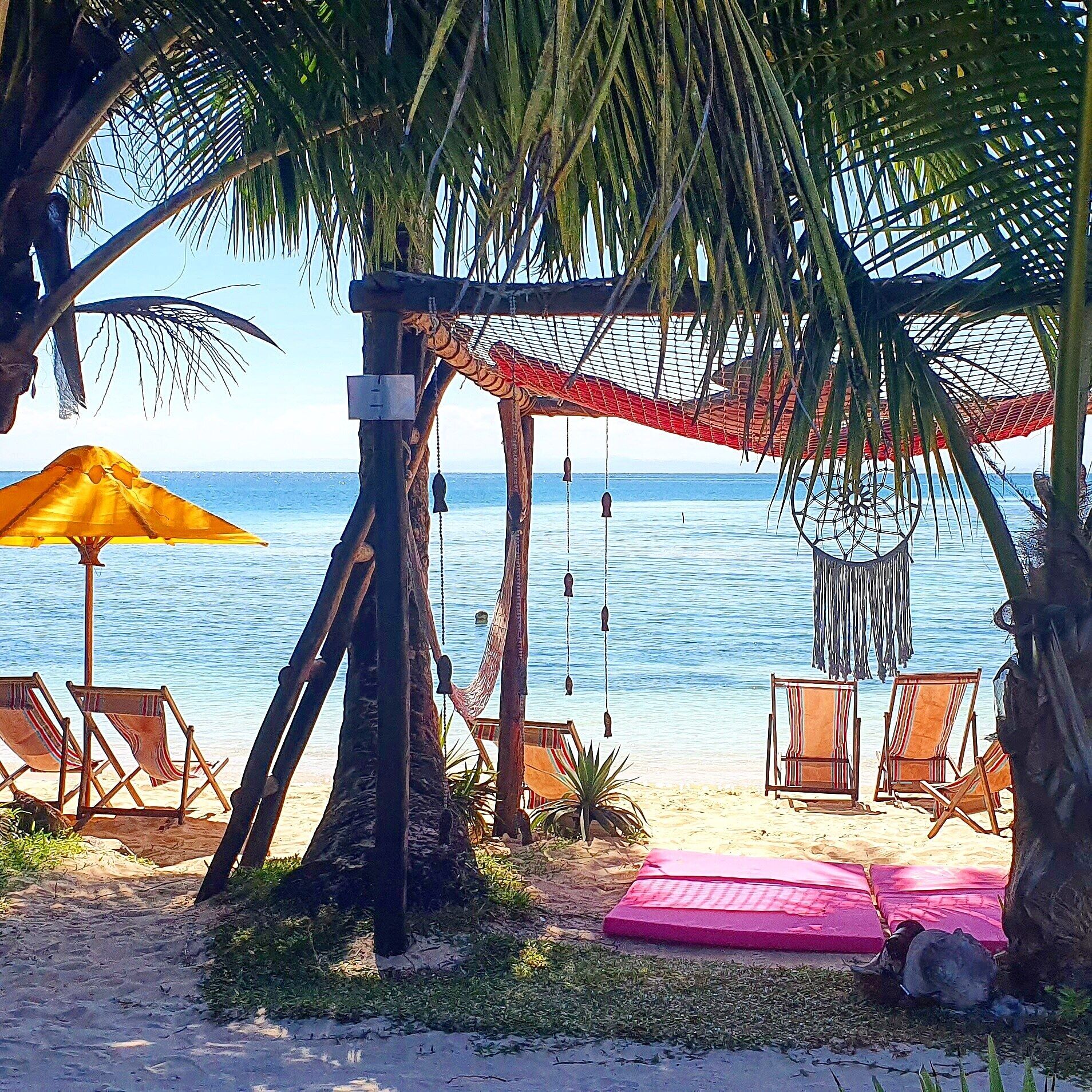 A beach scene with a hammock, lounge chairs, and a beach umbrella.