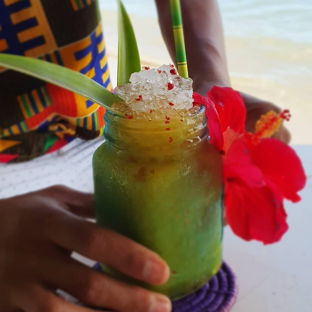 A person holding a drink with a green straw and a red flower garnish.