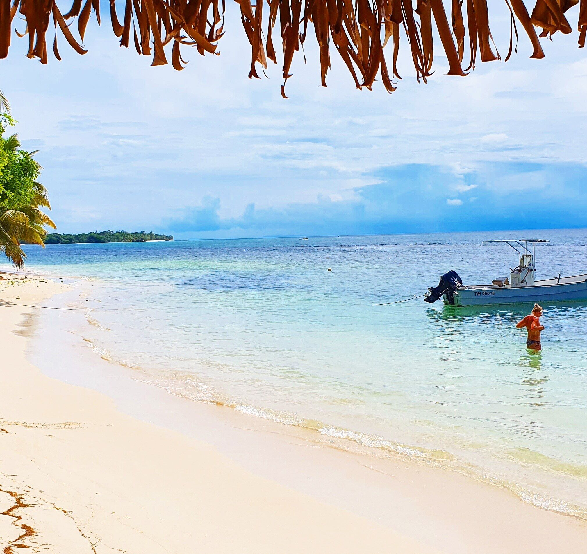 A beach with clear turquoise water, a boat, and a person in the water.