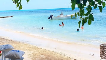 Ein Strand mit klarem, blauen Wasser, Menschen beim Schwimmen und ein Schiff in der Ferne.