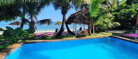 A pool area with lounge chairs and umbrellas, surrounded by palm trees and a view of the ocean.