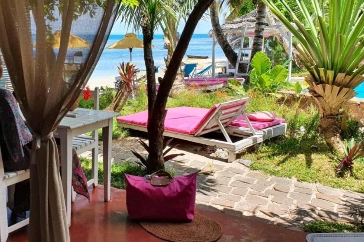 A room with a view of the beach, a table with a chair, a pink cushion, and a potted plant.