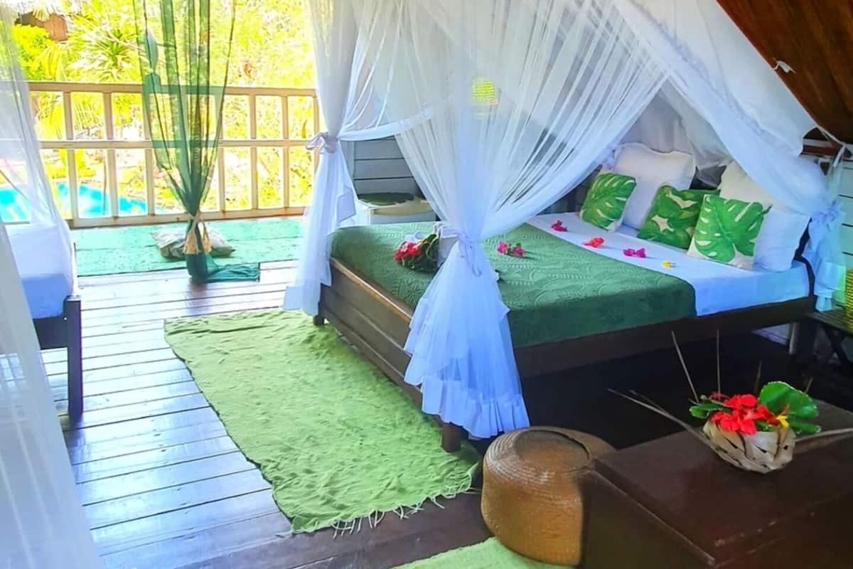 A room with a bed under a white canopy, green bedding, and a wooden floor.