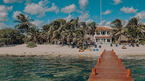 A wooden pier leading to a beach with palm trees and a building with a red roof. - Casa Altamar (Tulum)