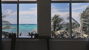 Una habitación con dos ventanas amplias que dan a una playa con palmeras y el océano.