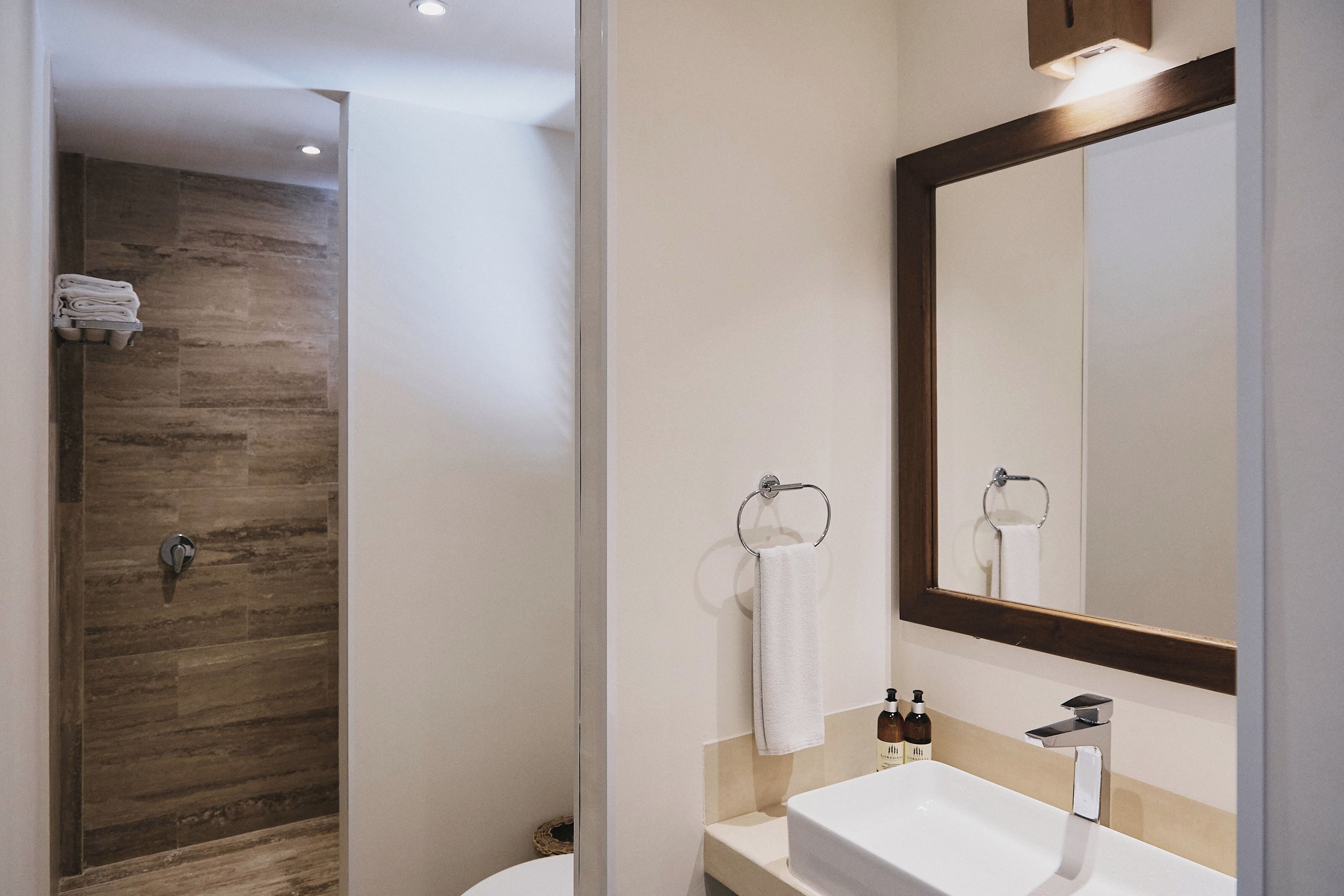 Un baño moderno con pared de ducha de madera, un lavabo blanco y un espejo grande.