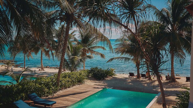 Zona de piscina con sillones, palmeras y vista al océano.