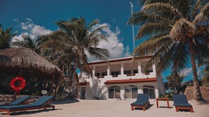 Un hotel frente a la playa con fachada blanca, varios balcones y palmeras.