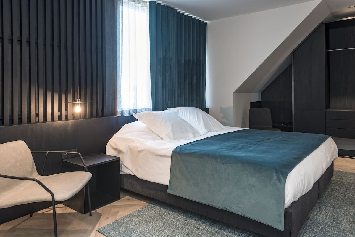 Een moderne slaapkamer met een bed, een stoel, een bureau en een groot raam met gordijnen.