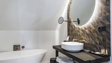 A modern bathroom with a freestanding bathtub, a round mirror, and a vanity with a geometric-patterned backsplash.
