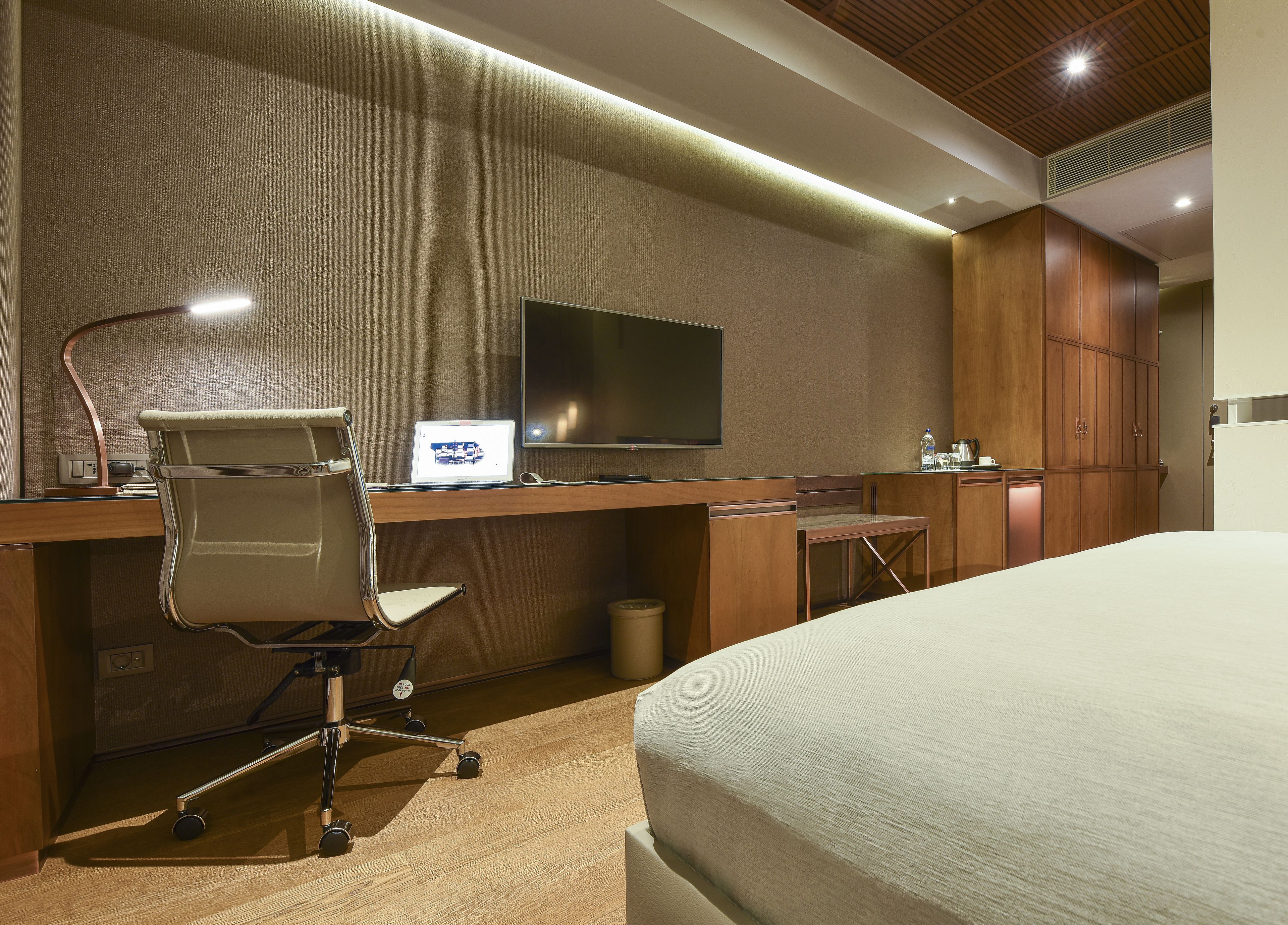 A hotel room with a bed, a desk with a laptop, a chair, a television, and wooden cabinets.