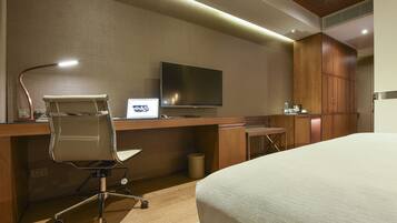 A hotel room with a bed, a desk with a laptop, a chair, a television, and wooden cabinets.
