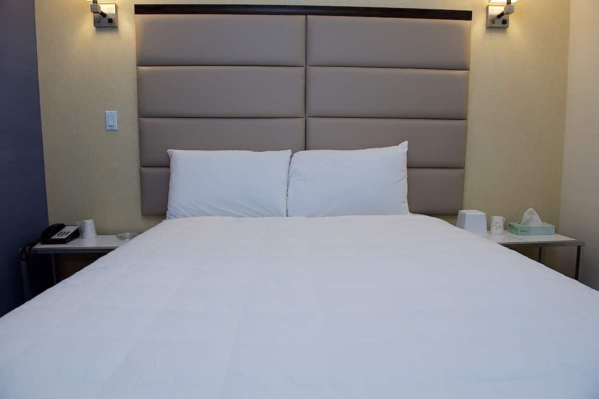 A hotel room with a large bed, a headboard, a bedside table with a phone, a tissue box, and a cup.
