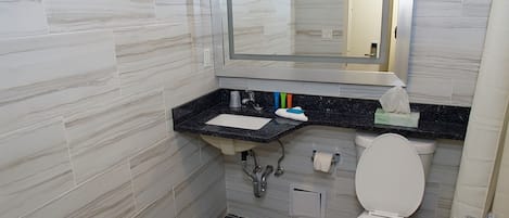 A bathroom with a marble backsplash, a sink with a mirror above it, a toilet, and a towel dispenser.