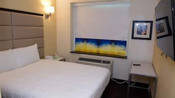 Habitación de hotel con una cama grande, una mesita de noche, aire acondicionado instalado en la pared, una pequeña mesa y un cuadro enmarcado.