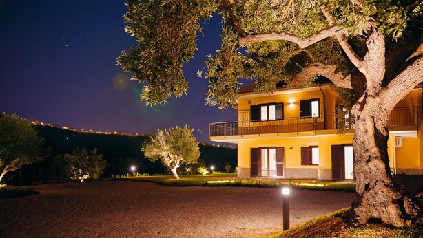 A two-story building with a balcony, surrounded by trees and a gravel driveway at night. - Cilentia B&B (Agropoli)
