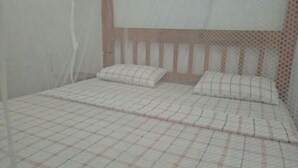 A bed with a checkered bedspread and two pillows, a white mosquito net, and a headboard with a patterned design. - Vosteen Home Holidays (Watamu)