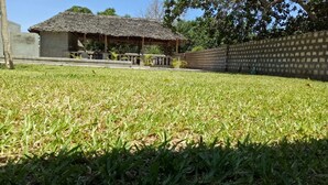 A grassy area with a thatched-roof structure and a brick wall. - Vosteen Home Holidays (Watamu)