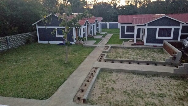 A row of small, uniformly designed cabins with red roofs, arranged in a linear fashion along a paved pathway. - Vosteen Home Holidays (Watamu)