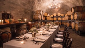 Una lunga tavola imbandita per la cena in una cantina con botti di vino sullo sfondo.