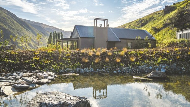 Una casa moderna con un camino centrale, circondata da un giardino e un piccolo stagno.