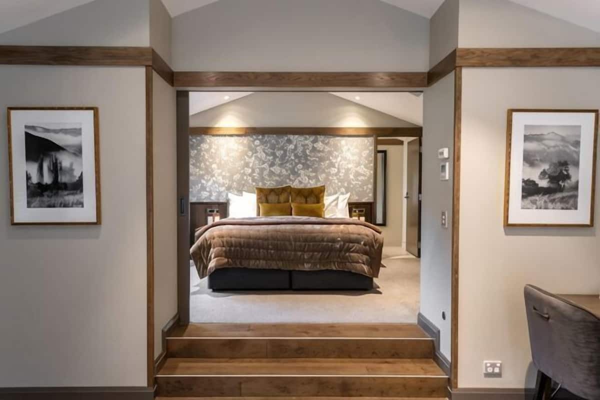 A bedroom with a large bed, a wooden staircase, and framed pictures on the walls.