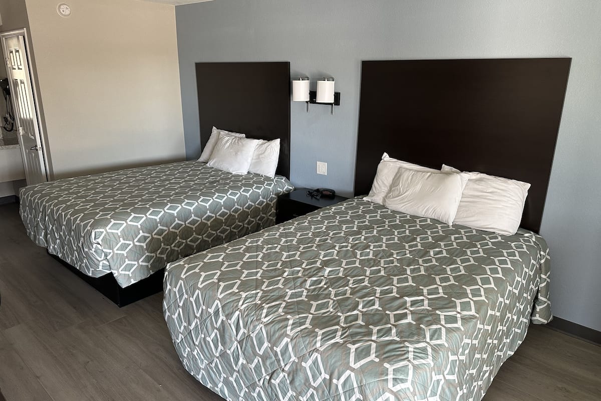Two twin beds with geometric-patterned bedding in a hotel room with a dark headboard and light walls.