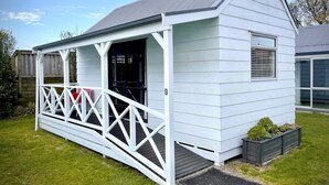 A small, white wooden structure with a porch and a window. - Pacific Park Christian Holiday Camp (Tauranga)