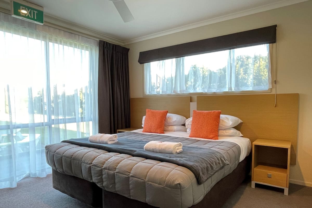 A hotel room with a large bed, two pillows, a bedside table, and a window with curtains.