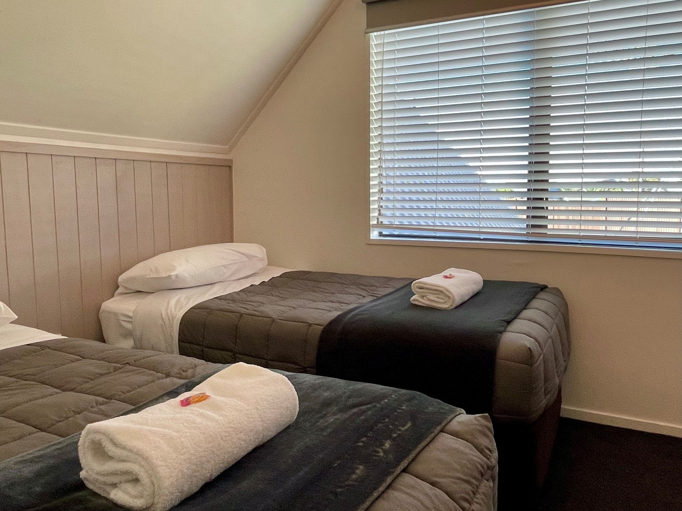 A hotel room with two beds, a window with blinds, and a wooden headboard.