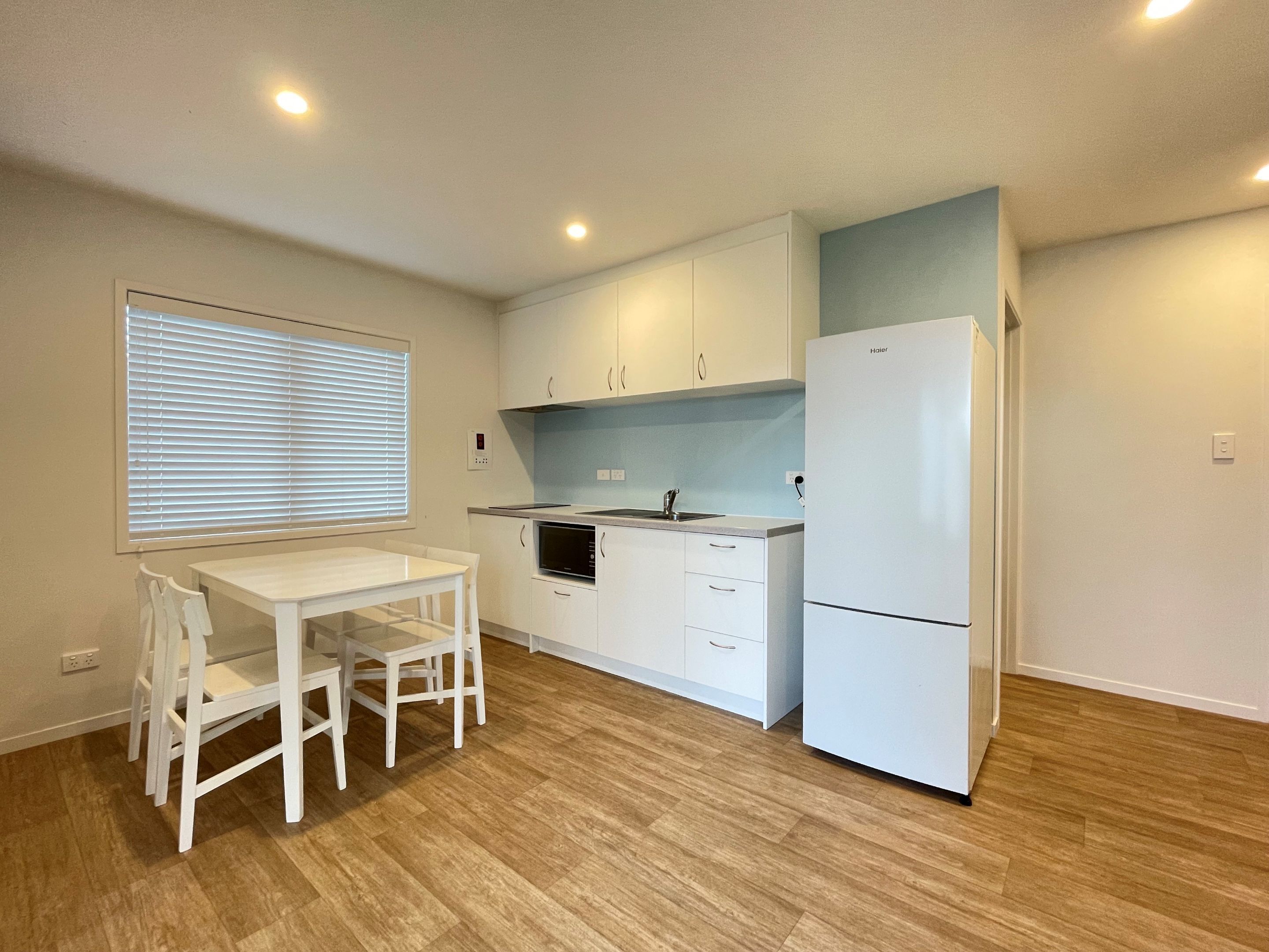 Cocina compacta con armarios blancos, horno empotrado, refrigerador y una mesa de comedor con sillas.