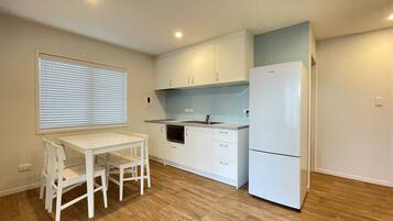 Cocina compacta con armarios blancos, horno empotrado, refrigerador y una mesa de comedor con sillas.